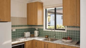 A kitchen with wooden cabinets, a white refrigerator, a sink, a window, and a countertop with a toaster, kettle, and a bowl of fruit.