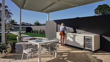 An outdoor kitchen area with a built-in grill, a dining table with chairs, and a covered patio.
