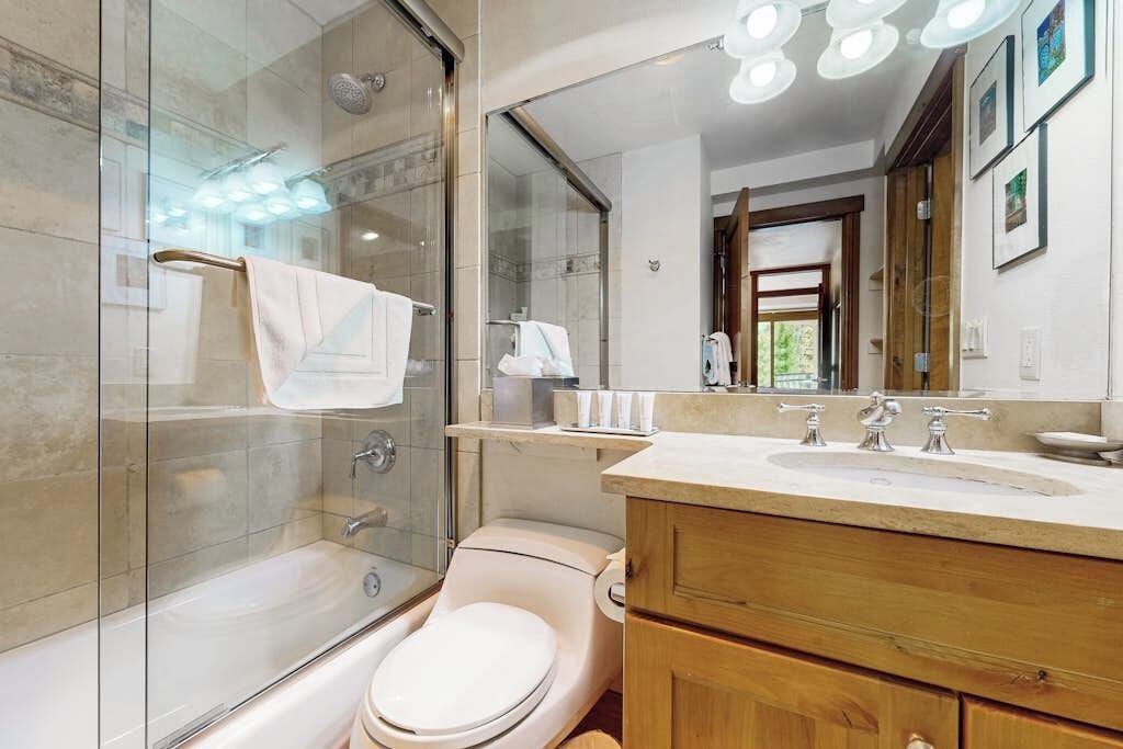 A modern bathroom with a glass-enclosed shower, a toilet, a sink with a vanity, and a large mirror.