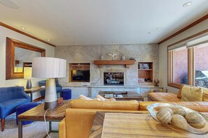 Ein modernes Wohnzimmer mit Kamin aus Stein, bequemen Sitzmöglichkeiten und einem Fernseher.
