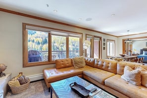 Ein Wohnzimmer mit einer großen Eckcouch, einem Couchtisch und Blick auf einen Wald durch große Fenster.