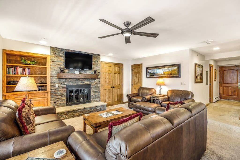 A living room with leather sofas, a fireplace, a television, and a ceiling fan.