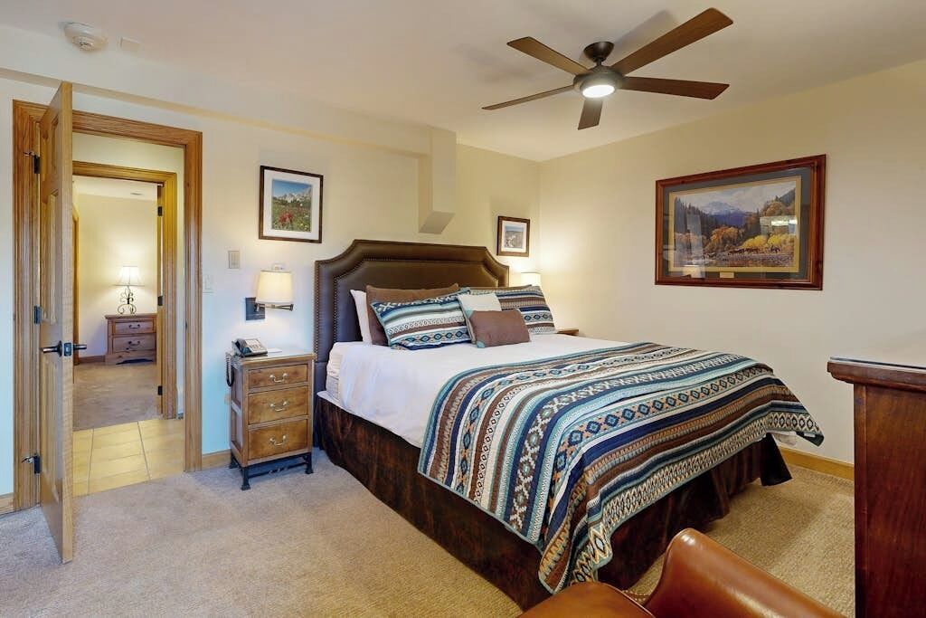 A bedroom with a bed, a nightstand, a dresser, a ceiling fan, and framed pictures on the walls.