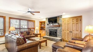 Ein Wohnzimmer mit Ledersofas, einem Kamin, Holzregalen und einem Deckenventilator.