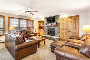 Ein Wohnzimmer mit Ledersofas, einem Kamin, Holzregalen und einem Deckenventilator.