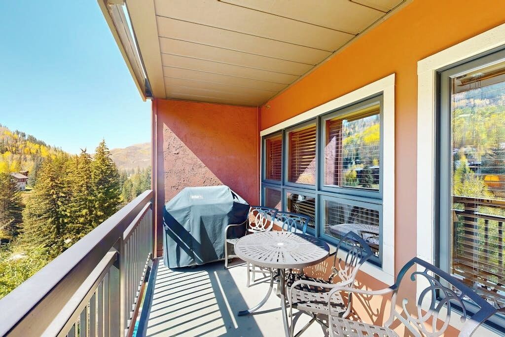 Ein Balkon mit Tisch, Stühlen, einem Grill und Blick auf eine bewaldete Gegend.