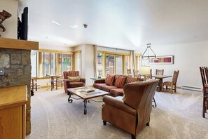 Ein geräumiges Wohnzimmer mit Kamin aus Stein, Ledersofas, einem Couchtisch und einem Essbereich mit Holzsesseln und Tisch.