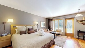 Quarto de hotel com uma cama grande, mesas de cabeceira, uma escrivaninha, um sofá e vista para o exterior pelas janelas.