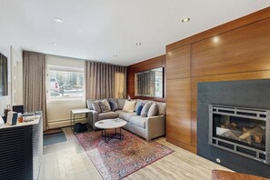 Ein modernes Wohnzimmer mit einer Eckcouch, einem Kamin, einem kleinen Tisch und einem großen Fenster mit Vorhängen.