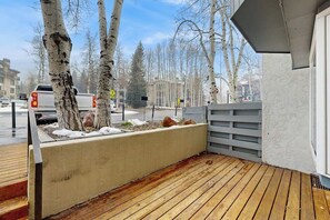 Eine Holzterrasse mit Birken, einem Betonpflanzgefäß und einem grauen Zaun.