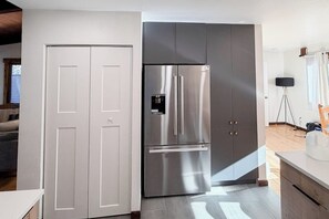 Eine moderne Küche mit einem Edelstahlkühlschrank, grauen Schränken und einer weißen Tür.