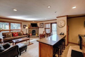 A spacious living room with a fireplace, a large dining area, and a kitchen with a bar. - Ski-in/out, mountain view condo w/ fireplace, fast WiFi, shared hot tubs/pool/WD (Vail)