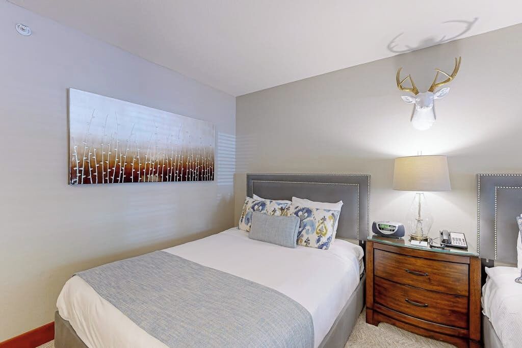 A hotel room with a bed, bedside table, lamp, and a wall-mounted deer head decoration.