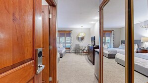 Une chambre d’hôtel avec une porte en bois, un bureau avec une chaise, deux lits, une télévision et un miroir.
