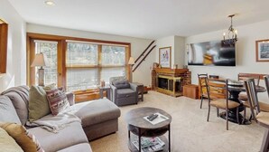 Ein Wohnzimmer mit Sofa, Sessel, Couchtisch, Kamin, Fernseher und Essbereich.