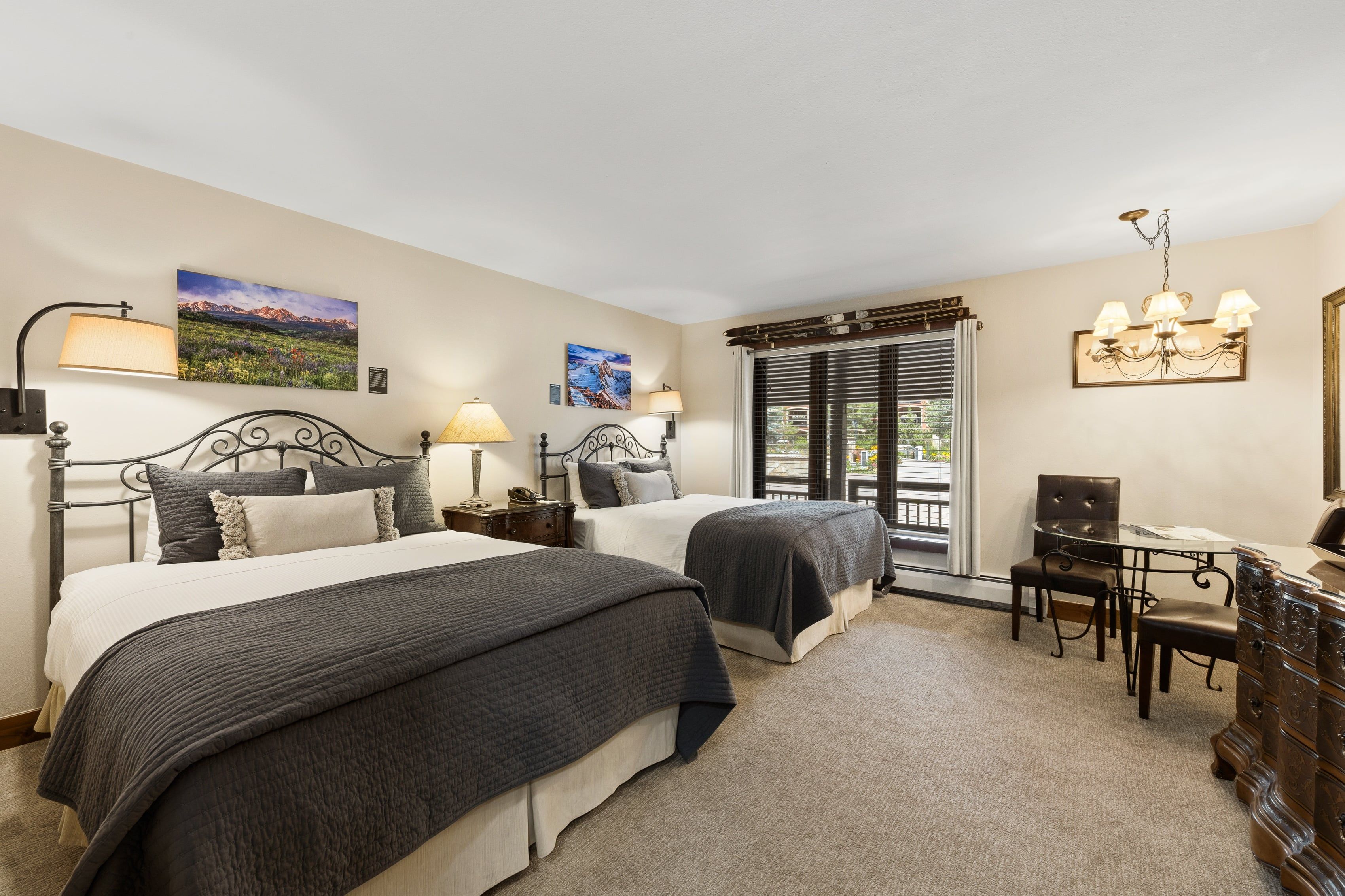 A hotel room with two beds, a desk with a chair, and a window with blinds.