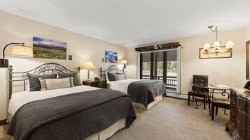 A hotel room with two beds, a desk with a chair, and a window with blinds.