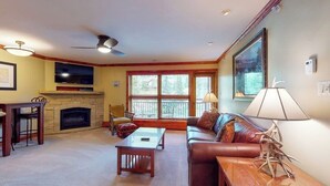 A living room with a fireplace, a sofa, a coffee table, and a TV. - Ski-in/out, mountain view condo w/ fireplace, fast WiFi, shared pool/WD/hot tub (Vail)