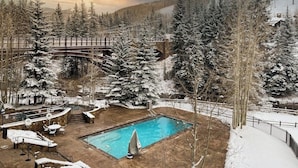 A pool area with a wooden deck, lounge chairs, and a small pool surrounded by snow-covered trees and a mountain backdrop. - Ski-in/out, mountain view condo w/ fireplace, fast WiFi, shared pool/WD/hot tub (Vail)