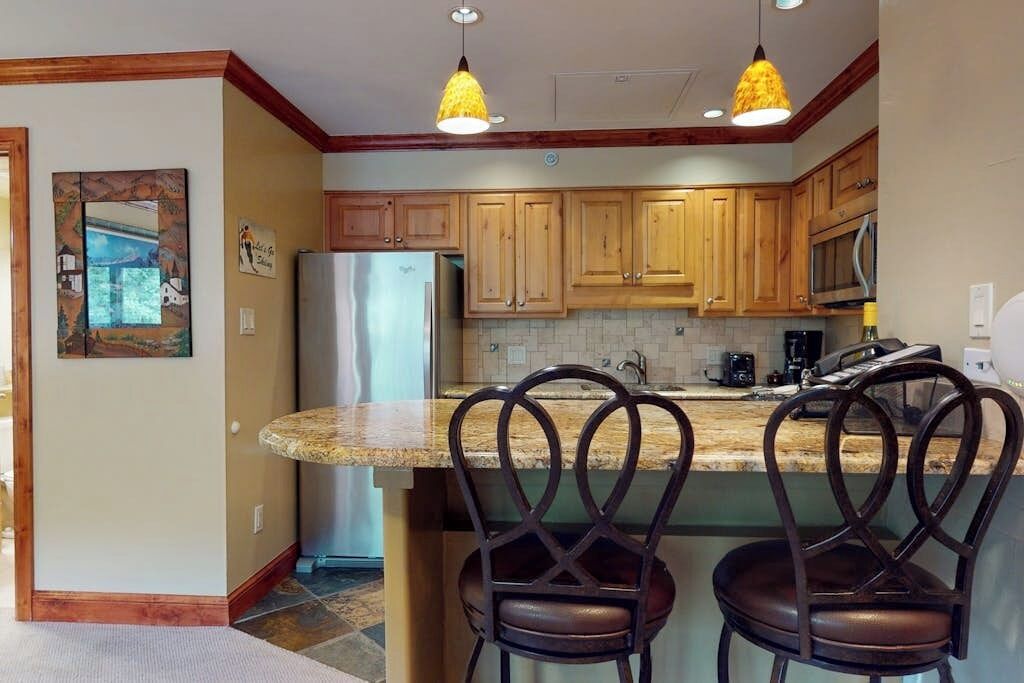 A kitchen with wooden cabinets, a stainless steel refrigerator, and a granite countertop.