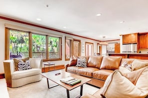 A spacious living area with a sofa, coffee table, and a view of the outdoors through large windows. - Ski-in/out condo w/ mountain view, fireplace, fast WiFi, shared pool/hot tubs/WD (Vail)