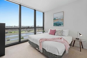 Ein Schlafzimmer mit großem Fenster, einem Bett, einem Nachttisch und einem Bild.