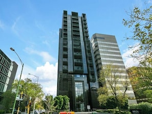 Een modern hoog gebouw met een glazen gevel, omgeven door bomen en andere gebouwen.