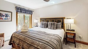 A bedroom with a bed, a ceiling fan, a window with a view, a bedside table, and a chair. - Mountain view, ski-in/out condo w/ fast WiFi, fireplace, shared pool/hot tubs/WD (Vail)