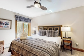 A bedroom with a bed, a ceiling fan, a window with a view, a bedside table, and a chair. - Mountain view, ski-in/out condo w/ fast WiFi, fireplace, shared pool/hot tubs/WD (Vail)