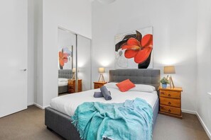 A bedroom with a bed, a mirror, two bedside tables with lamps, and a large abstract painting on the wall. - Xavier - Best location in Melbourne with Parking! (Melbourne)