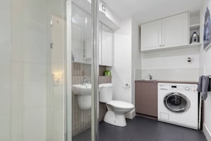 A modern bathroom with a glass shower enclosure, a toilet, a sink, and a built-in washing machine. - Xavier - Best location in Melbourne with Parking! (Melbourne)