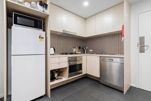 A modern kitchen with a microwave, oven, and dishwasher, wooden cabinets, and a tiled backsplash. - Xavier - Best location in Melbourne with Parking! (Melbourne)