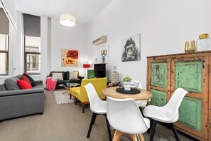 A modern living room with a sofa, yellow chair, dining table, and a cabinet with green doors. - Xavier - Best location in Melbourne with Parking! (Melbourne)