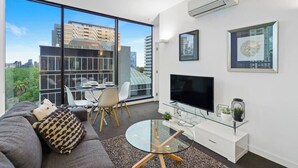 Una sala de estar moderna con un televisor grande, una mesa de centro de vidrio y un sofá.