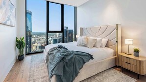 Un dormitorio moderno con una cama grande, una mesita de noche, una lámpara, una planta en maceta y vistas a la ciudad.