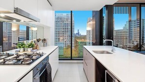 A modern kitchen with a large window, a gas stove, and a sink. - Charlie - Floor to Ceiling Views Stunner. Parking. (Melbourne)