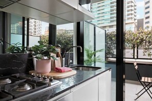A modern kitchen with a gas stove, a sink, and a window overlooking a cityscape. - Dee - Gorgeous modern apartment in perfect location (South Melbourne)