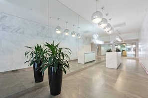 A modern lobby with marble walls, potted plants, and a reception desk. - Dee - Gorgeous modern apartment in perfect location (South Melbourne)