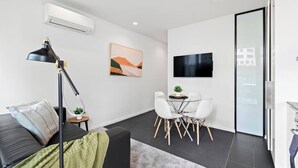 Una sala de estar moderna con un sofá, una mesa de comedor con sillas, un televisor y un equipo de aire acondicionado.
