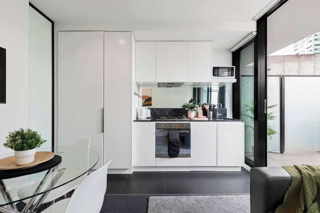 A modern kitchen with white cabinets, a microwave, and a stove. There is a glass door leading to an outdoor area.