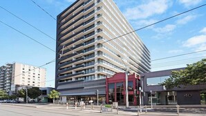Un edificio moderno de gran altura con varios pisos, amplias ventanas y una entrada destacada con toldo rojo.