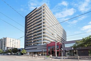 A modern high-rise building with multiple floors, large windows, and a prominent entrance with a red awning. - Dee - Gorgeous modern apartment in perfect location (South Melbourne)