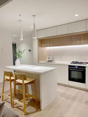 A modern kitchen with a central island, wooden chairs, a built-in oven, and pendant lighting. - Jaw-dropping views from executive city residence (Melbourne)