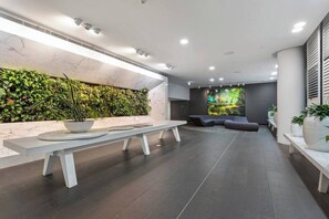 Eine moderne Lobby mit einer Marmor-Rezeption, einer vertikalen Grünwand, einer Sitzecke und einem großen Bildschirm.