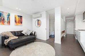 A modern living room with a black leather sofa, a round rug, and abstract paintings on the wall. - EDEN - Southbank Stunner with WIFI Parking (South Melbourne)