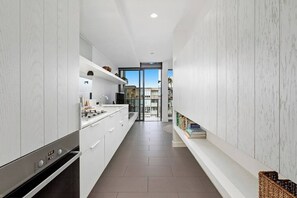 Eine schmale, moderne Küche mit weißen Schränken, einem eingebauten Ofen und einer Glastür, die auf einen Balkon führt.