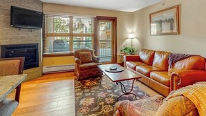 A living room with a fireplace, a sofa, a coffee table, and a TV mounted on the wall. - Ski-in/out, 4th-floor condo w/ fireplace, fast WiFi & shared hot tubs, pool, W/D (Vail)
