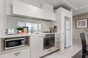 Eine moderne Küche mit weißen Schränken, einer Mikrowelle, einem Backofen, einer Spüle und einem Kühlschrank.