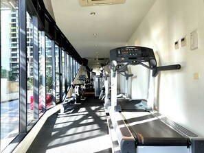 Ein Fitnessstudio mit Laufbändern, Kraftgeräten und einem großen Fenster mit Blick auf ein Gebäude.