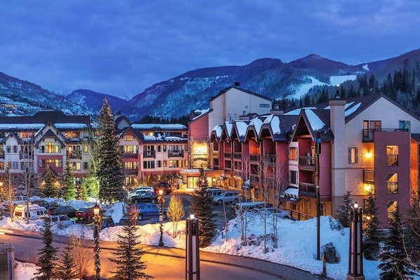 Ein Hotel mit mehreren Gebäuden, einem Parkplatz und verschneiten Bergen im Hintergrund.
